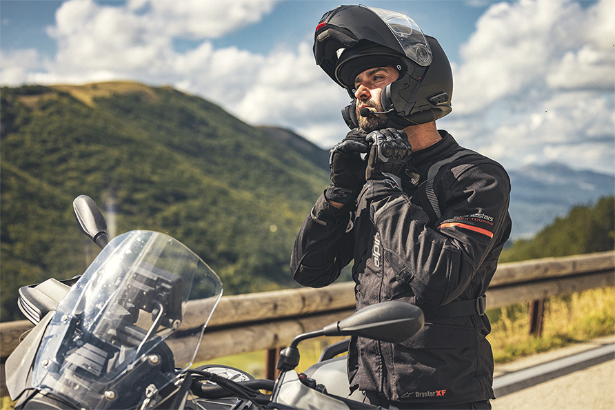 Helmsysteme_Partnerschaft-Schuberth | RUCH NOVAPLAST in Oberkirch Motorradfahrer steht neben einem Motorrad und schließt seinen Helm. Im Hintergrund sind Berg zu erkennen. | RUCH NOVAPLAST GmbH in Oberkirch